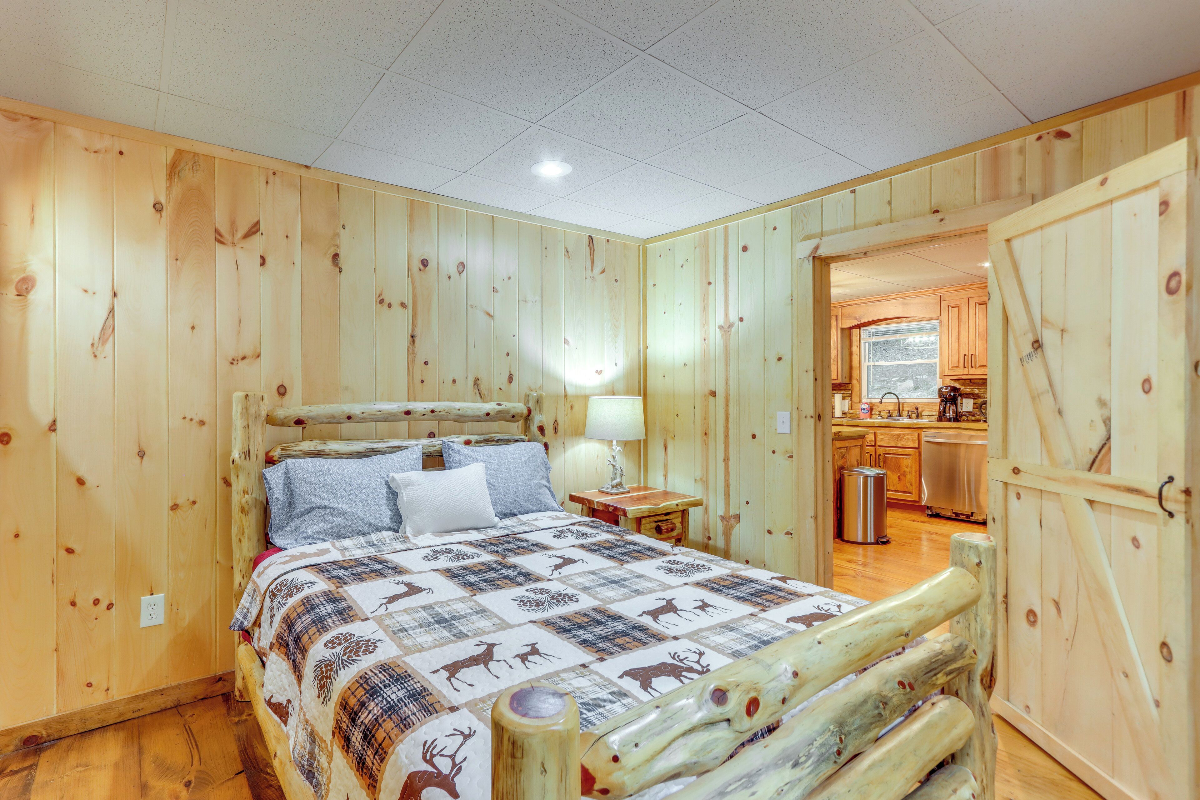 A wooden-paneled bedroom with a bed, a nightstand, and a view into a kitchen area.