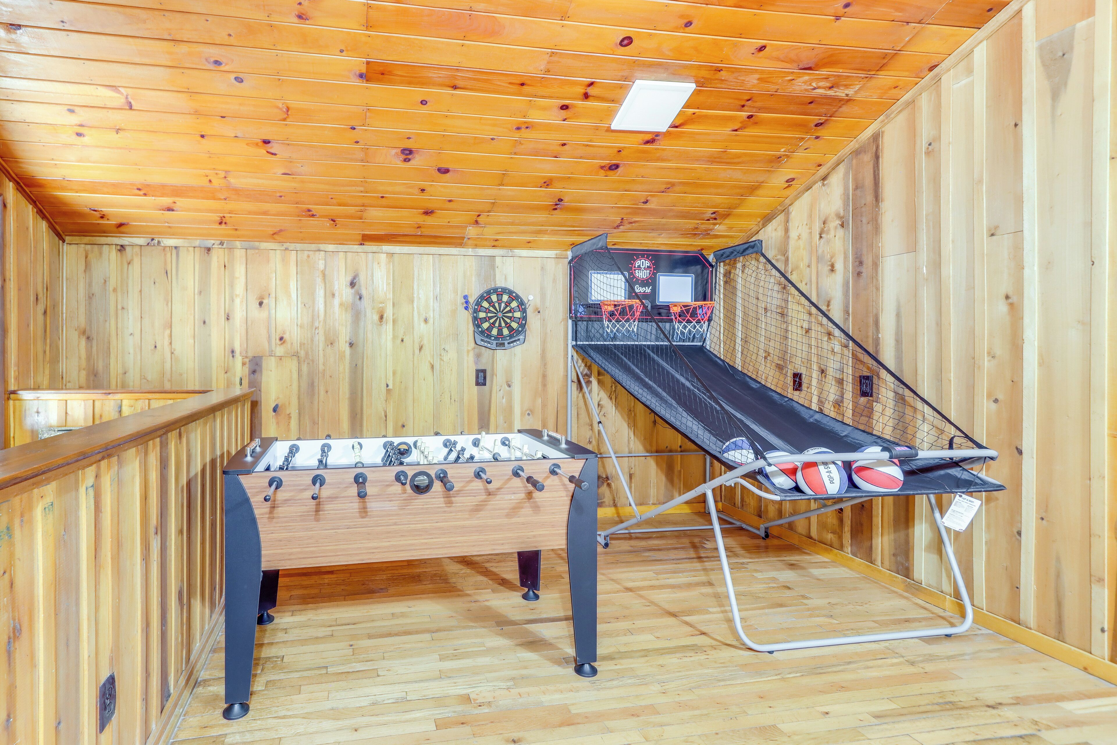 A room with a foosball table, a dartboard, and a basketball hoop.