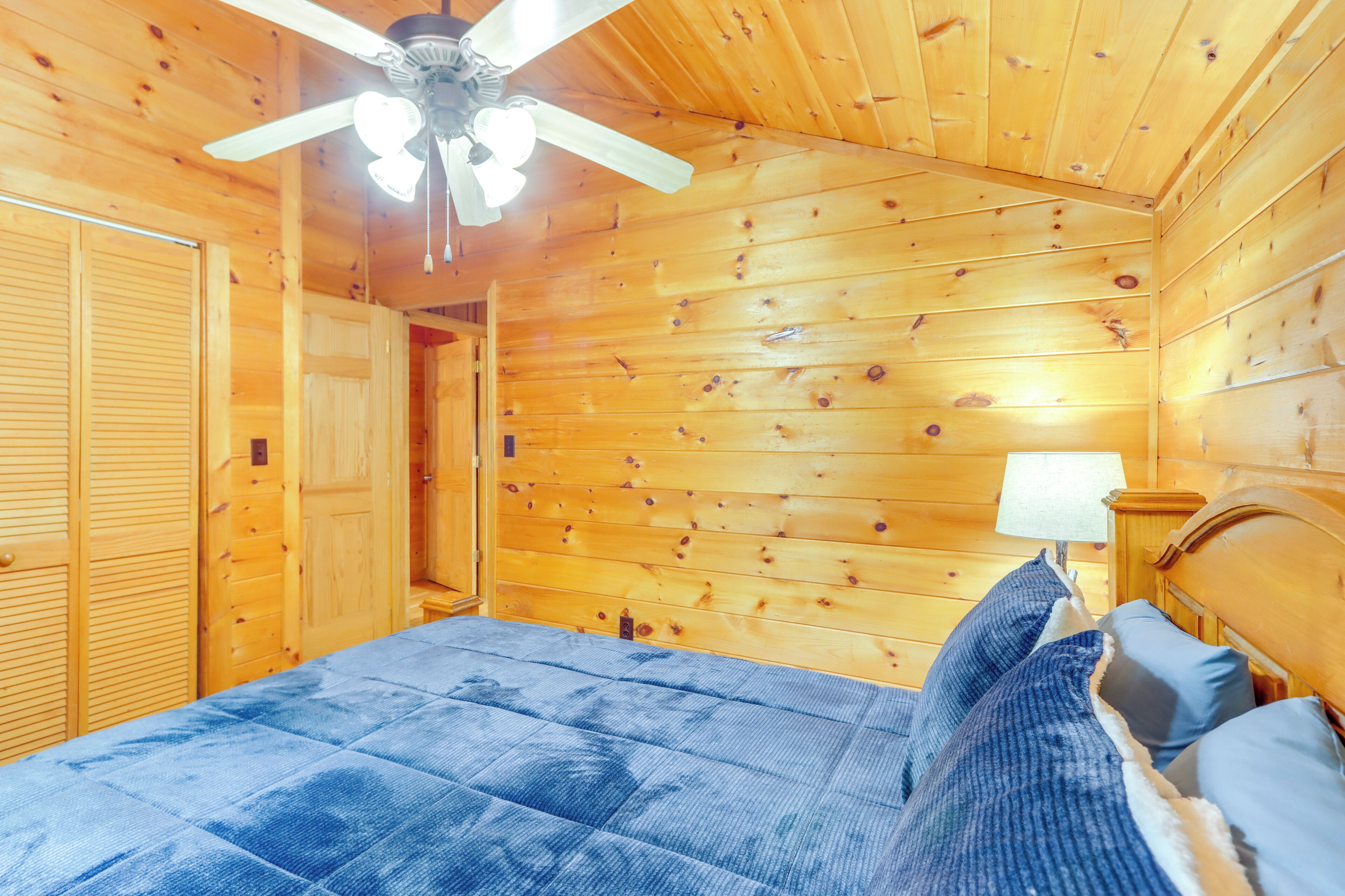A wooden cabin bedroom with a bed, a ceiling fan, and a nightstand.