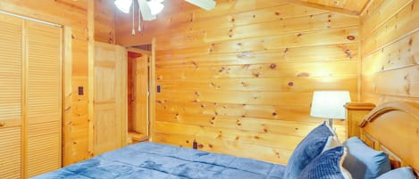 A wooden cabin bedroom with a bed, a ceiling fan, and a nightstand.