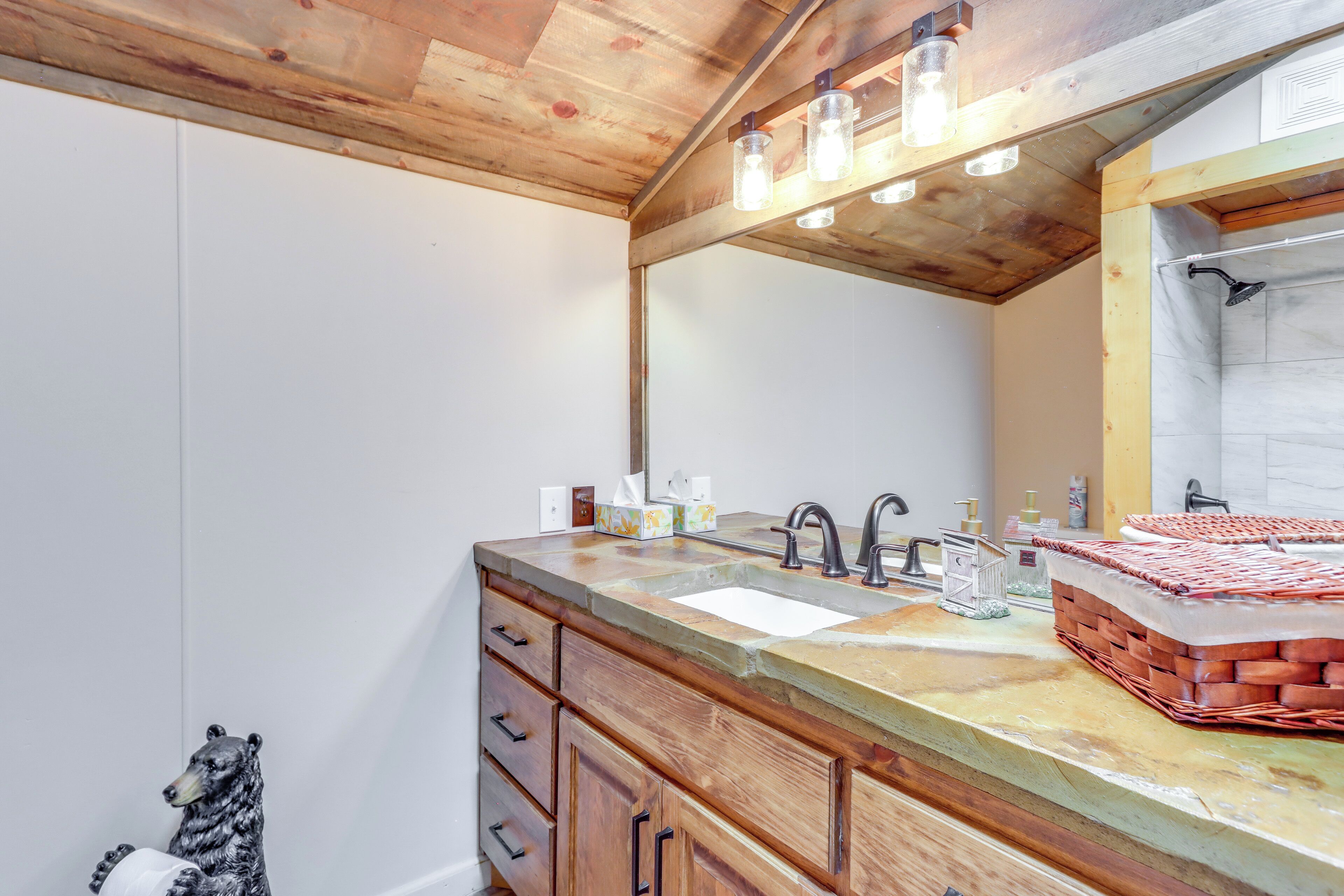 A bathroom with a wooden ceiling, a large mirror, a sink, and a towel rack.