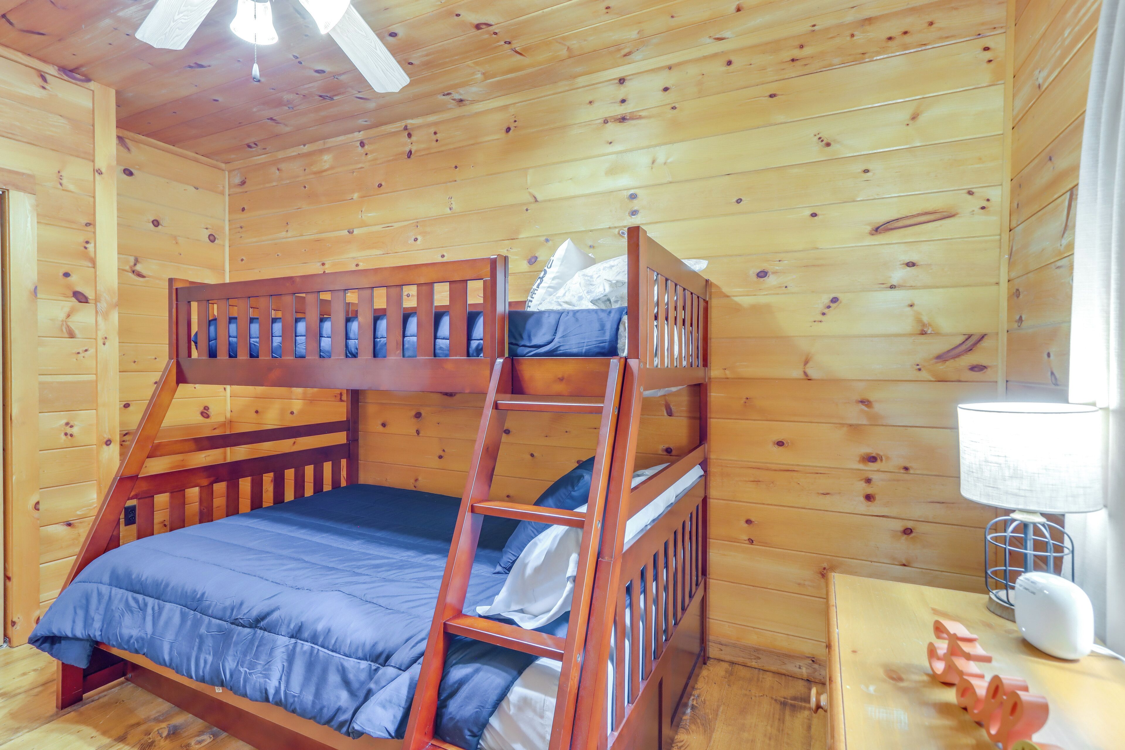 Uma cama beliche com colchão azul e cabeceira de madeira, num quarto de cabana com paredes e teto de madeira, e um ventilador.