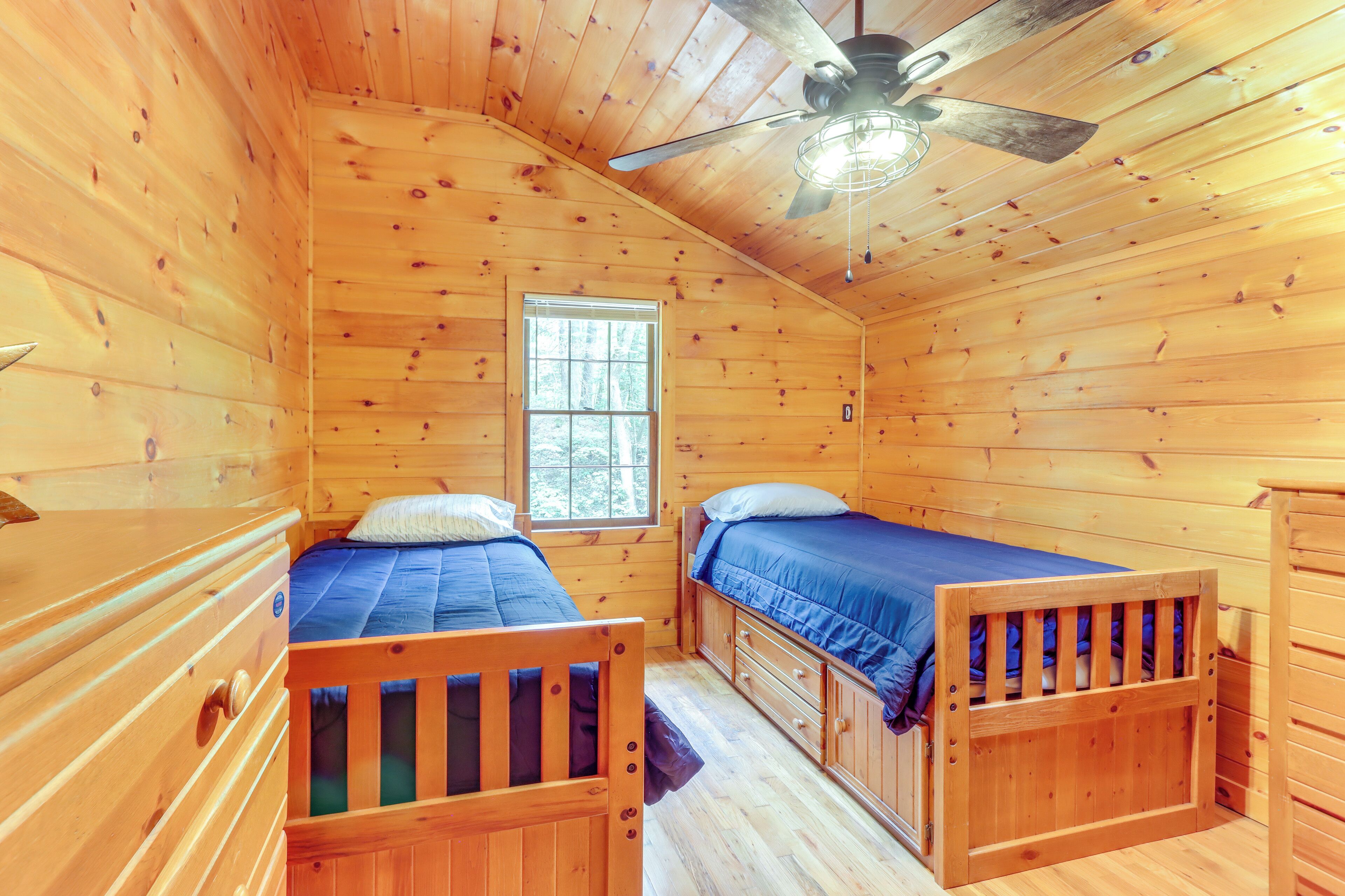 A cabin with two wooden bunk beds, a ceiling fan, and a window providing natural light.