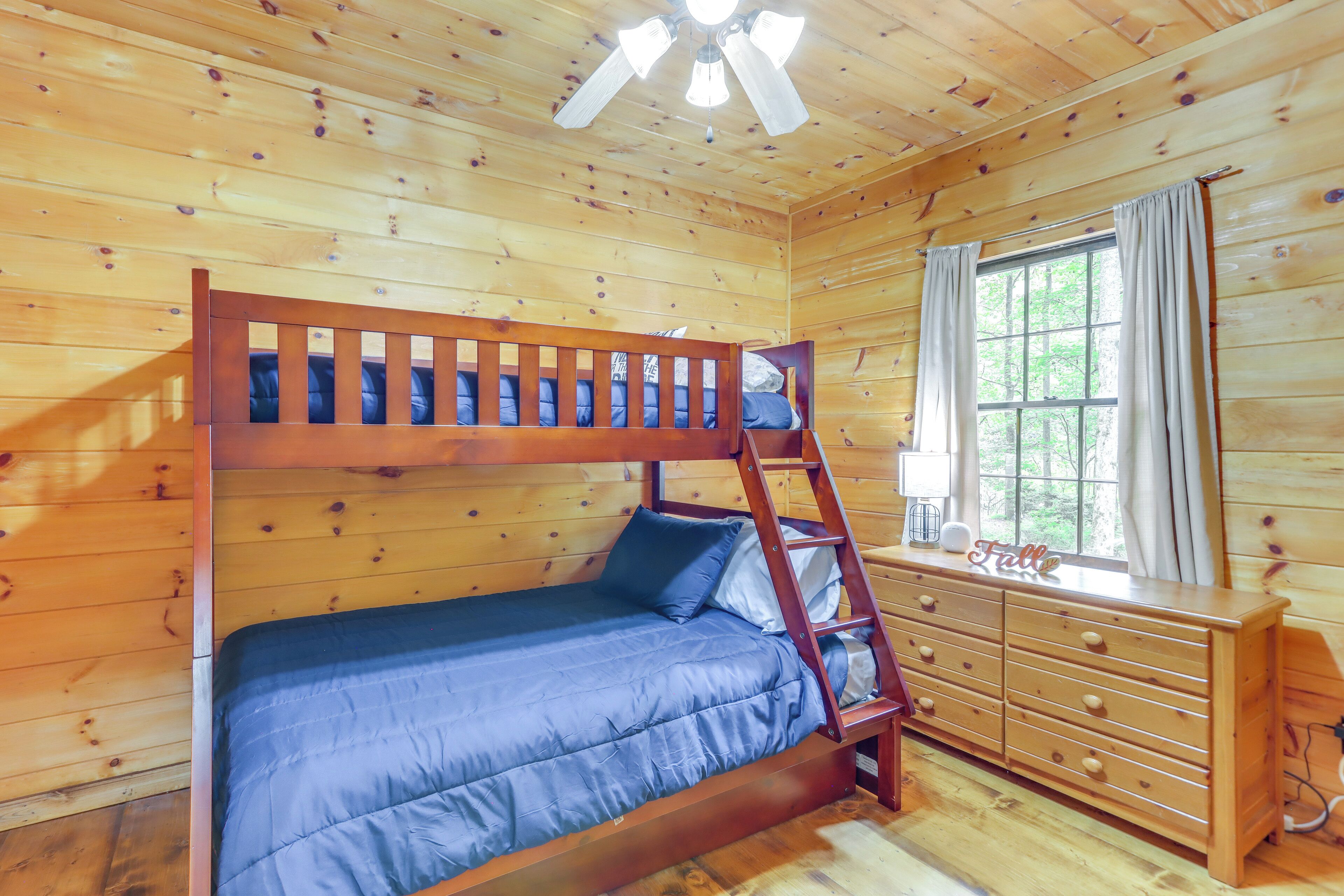 A wooden cabin room with a bunk bed, a dresser, and a window with curtains.