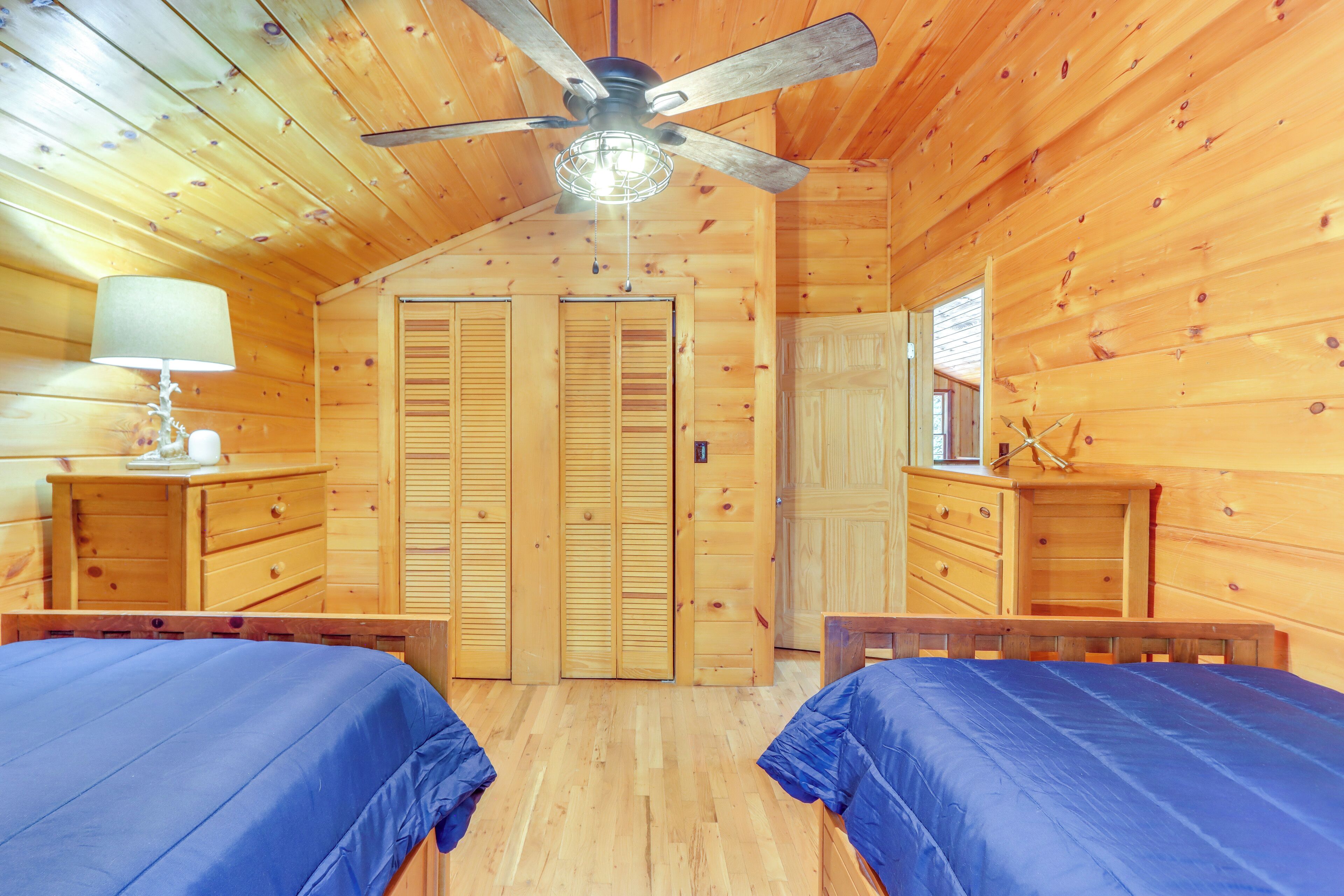 Un dormitorio de cabaña de madera con dos camas, un ventilador de techo y armarios de madera.