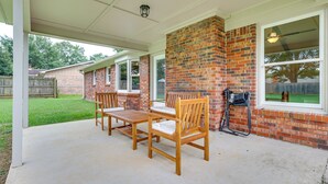 A covered patio with a brick wall, wooden furniture, and a window overlooking a backyard. - Decatur Vacation Rental w/ Patio! (Decatur)