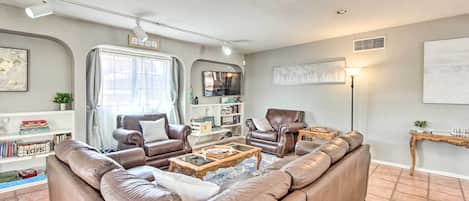Una sala de estar con un sofá modular, dos sillones, una mesa de centro, una estantería, un televisor y una lámpara.