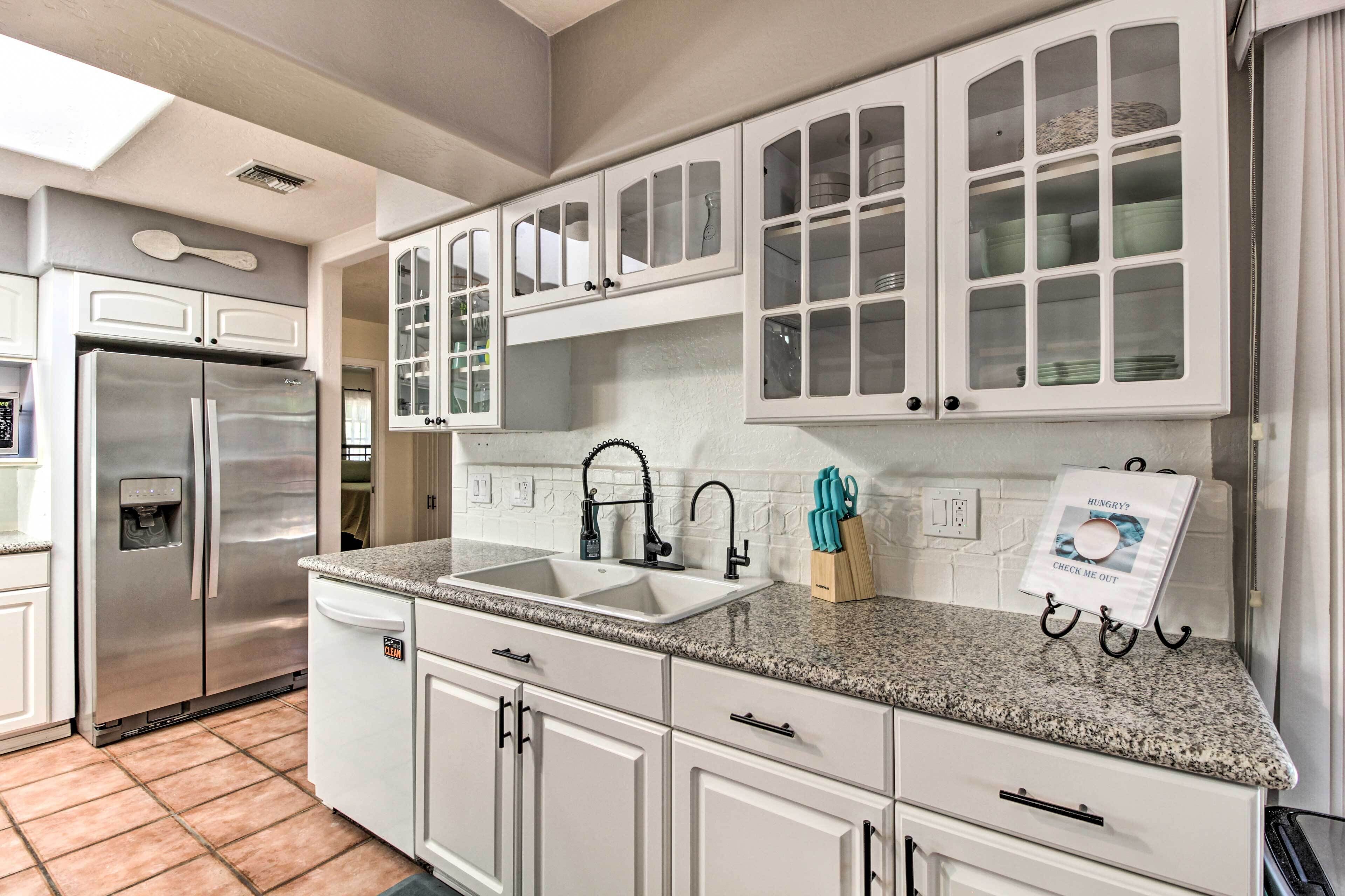 A kitchen with white cabinets, a stainless steel refrigerator, a granite countertop, and a window above the sink.