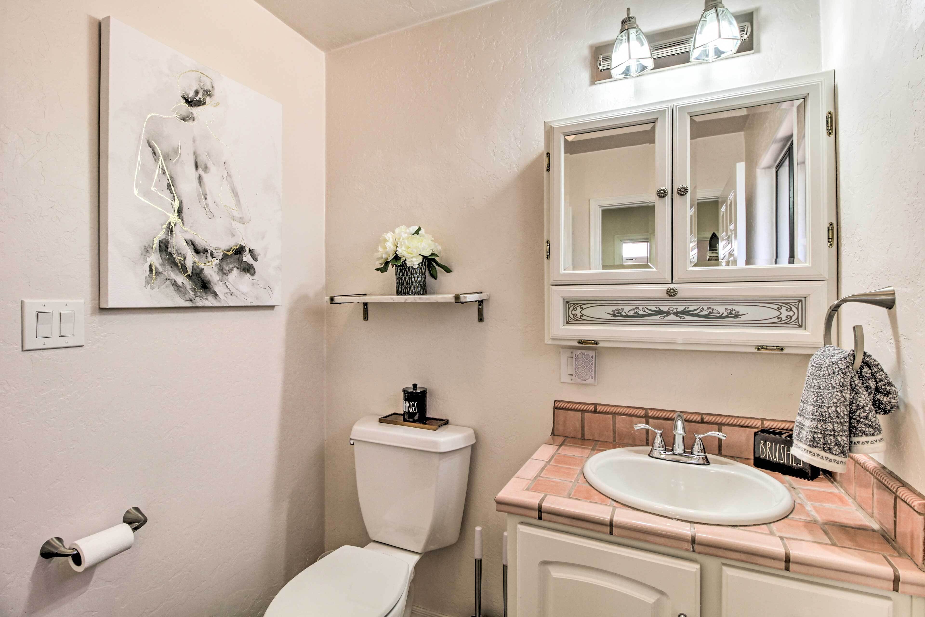 A bathroom with a toilet, sink, mirror, and a painting on the wall.