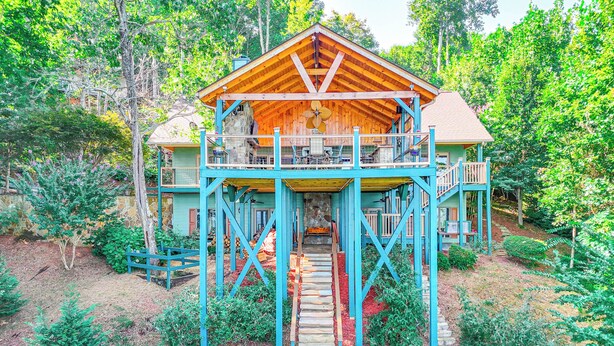A two-story wooden cabin with a balcony, surrounded by lush greenery.