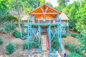 A two-story wooden cabin with a balcony, surrounded by lush greenery. - Hiawassee Home w/ Fire Pit & Furnished Deck! (Hiawassee)