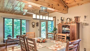 A dining area with a wooden ceiling, large windows, and a table set with floral tablecloths.