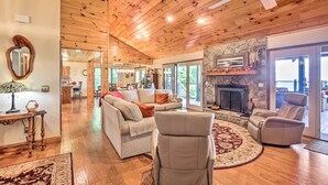 A spacious living room with a fireplace, wooden ceiling, and a view of the outdoors.