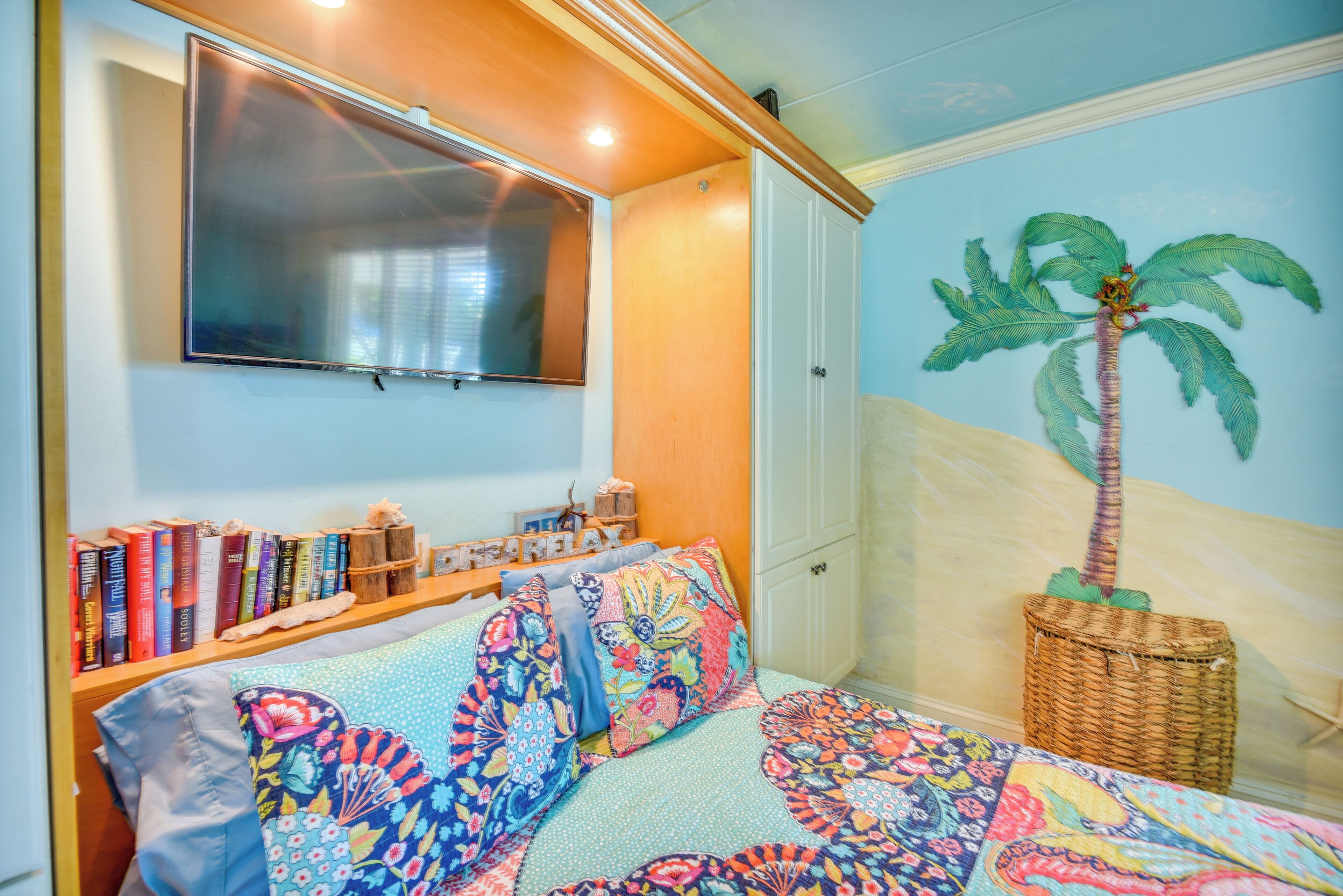 Un dormitorio con cama, estantería, televisor montado y un mural en la pared.