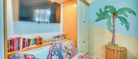 Un dormitorio con cama, estantería, televisor montado y un mural en la pared.