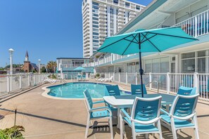 Un espace piscine avec des chaises longues et une table, le tout entouré d’une clôture blanche.