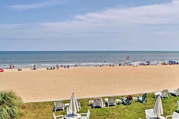 A beach with lounge chairs and umbrellas, a lifeguard tower, and people in the water.