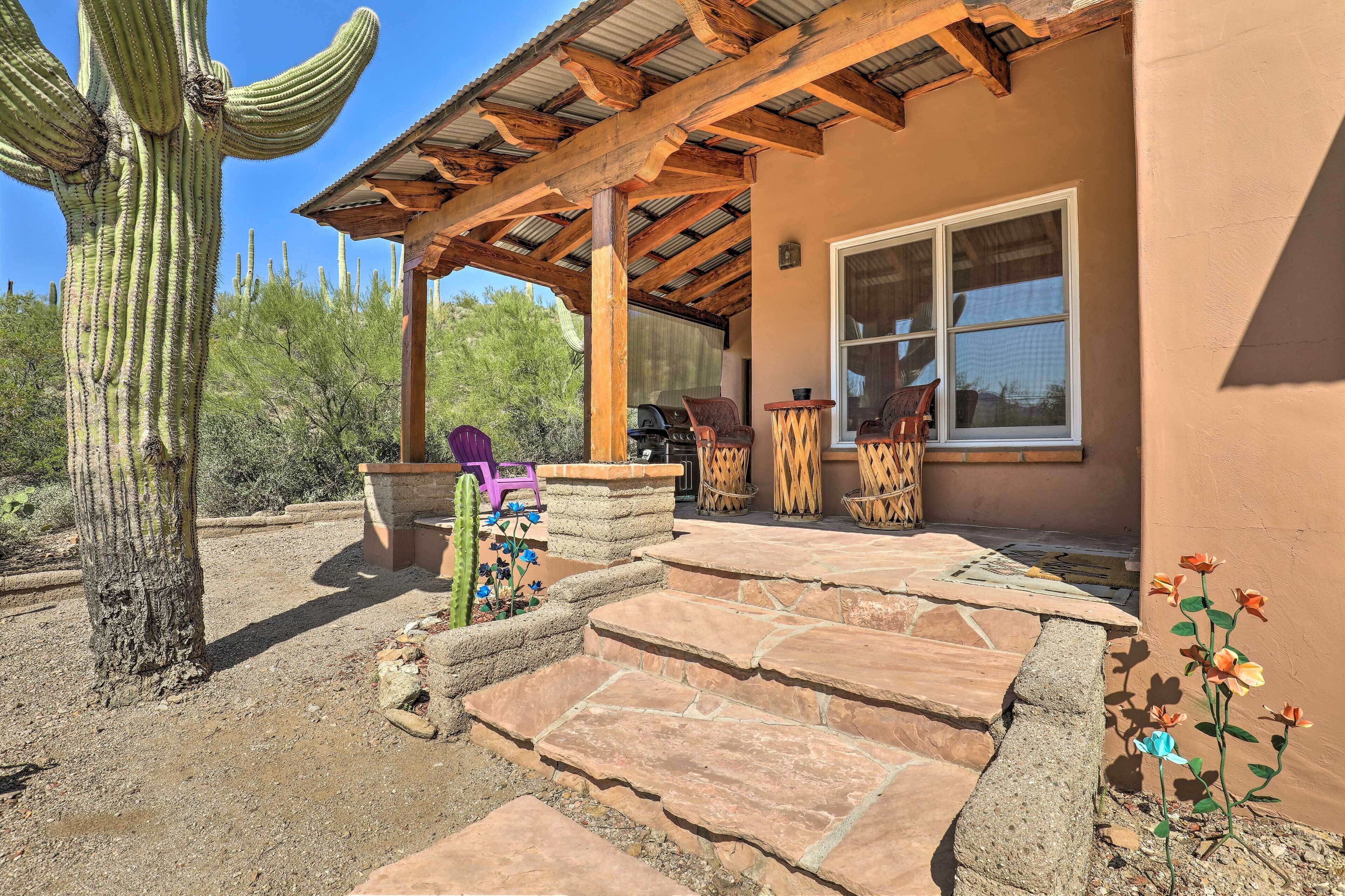 A covered patio with stone steps, wooden furniture, and a cactus in a desert setting.