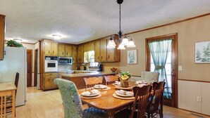 A spacious kitchen with wooden cabinets, a dining table set for four, and a central island with a sink and stove. - Cozy Georgia Getaway w/ Deck, Grill & Fire Pit! (Cartersville)