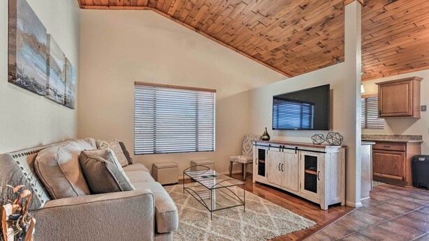 A spacious living area with a high ceiling, wooden beams, a sofa, a coffee table, a TV, and a kitchen area with cabinets and a countertop. - Fenced Yard & Grill! Tucson Family Escape (Tucson)
