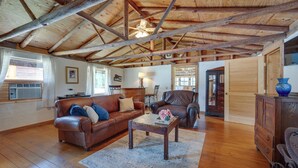 A spacious living room with wooden floors, a brown leather sofa, a wooden coffee table, and a large window. - Spacious Buena Vista Cabin w/ Lake Views & Deck (Buena Vista)