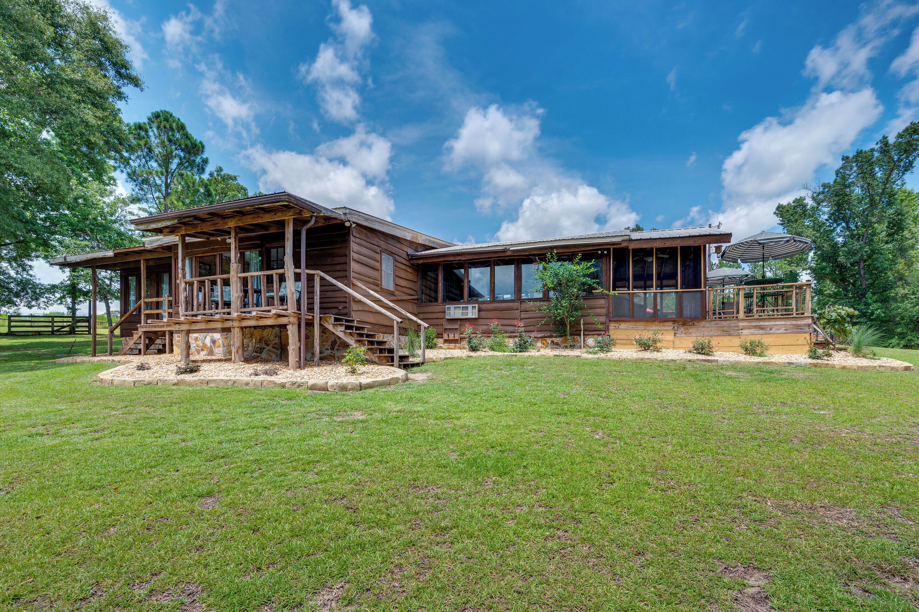 A two-story wooden house with a covered porch and a deck, surrounded by a well-maintained lawn and trees.