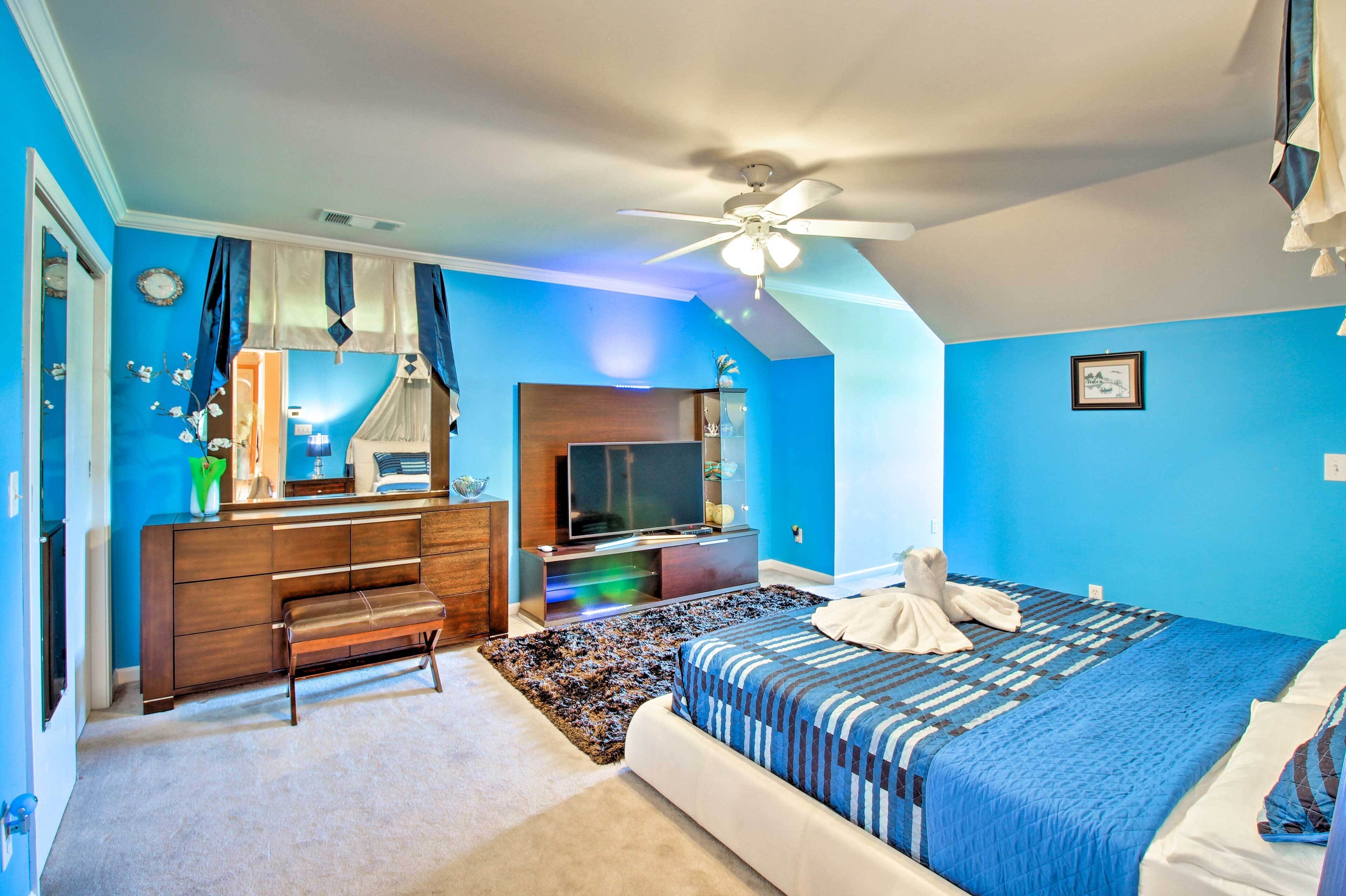 A bedroom with a bed, a vanity with a mirror, a television, and a ceiling fan.