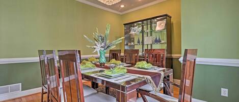 A dining room with a wooden table set for six, surrounded by chairs, a chandelier, and a decorative plant centerpiece.