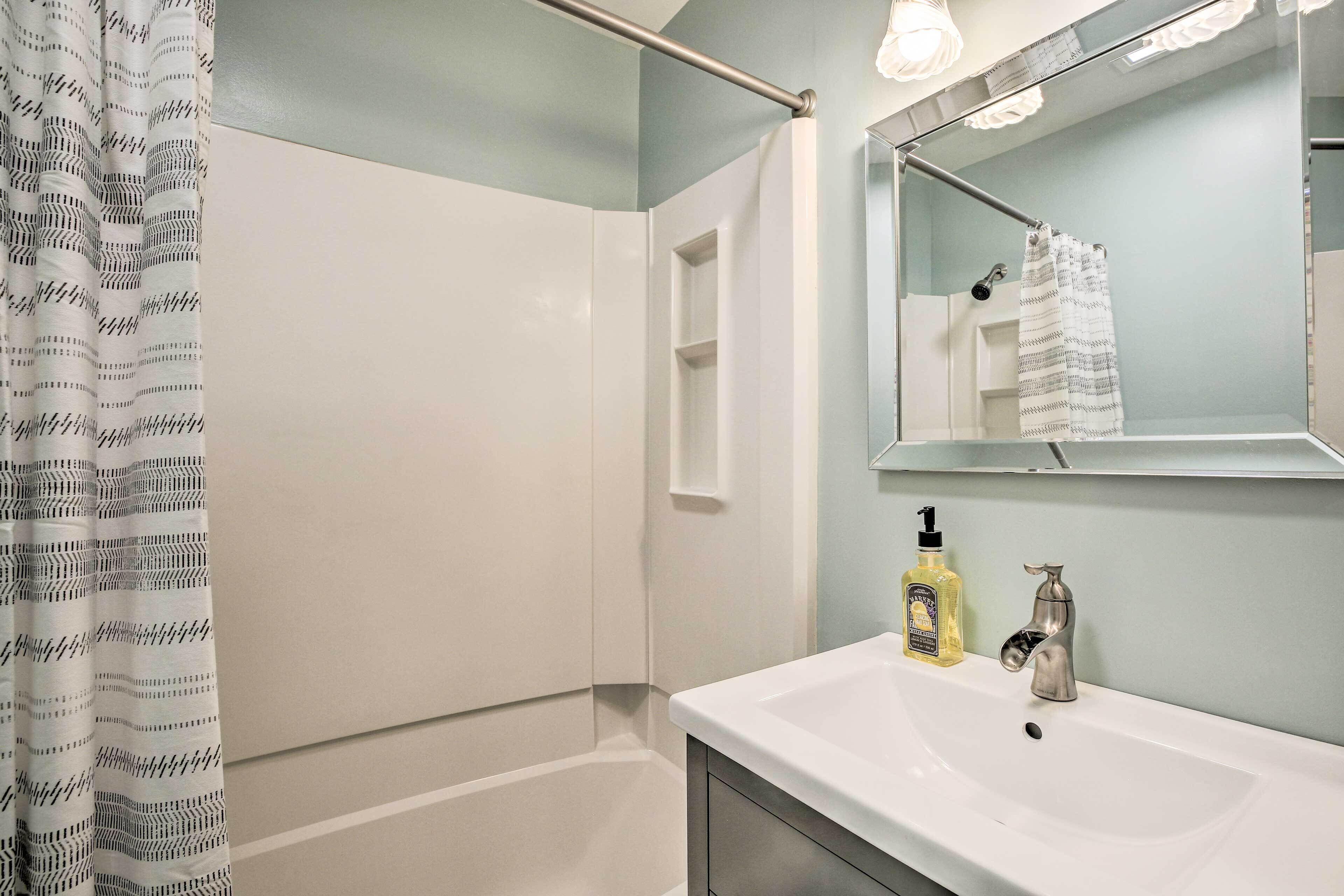 Een badkamer met een witte wastafel, een spiegel, een douche en een handdoekrek.