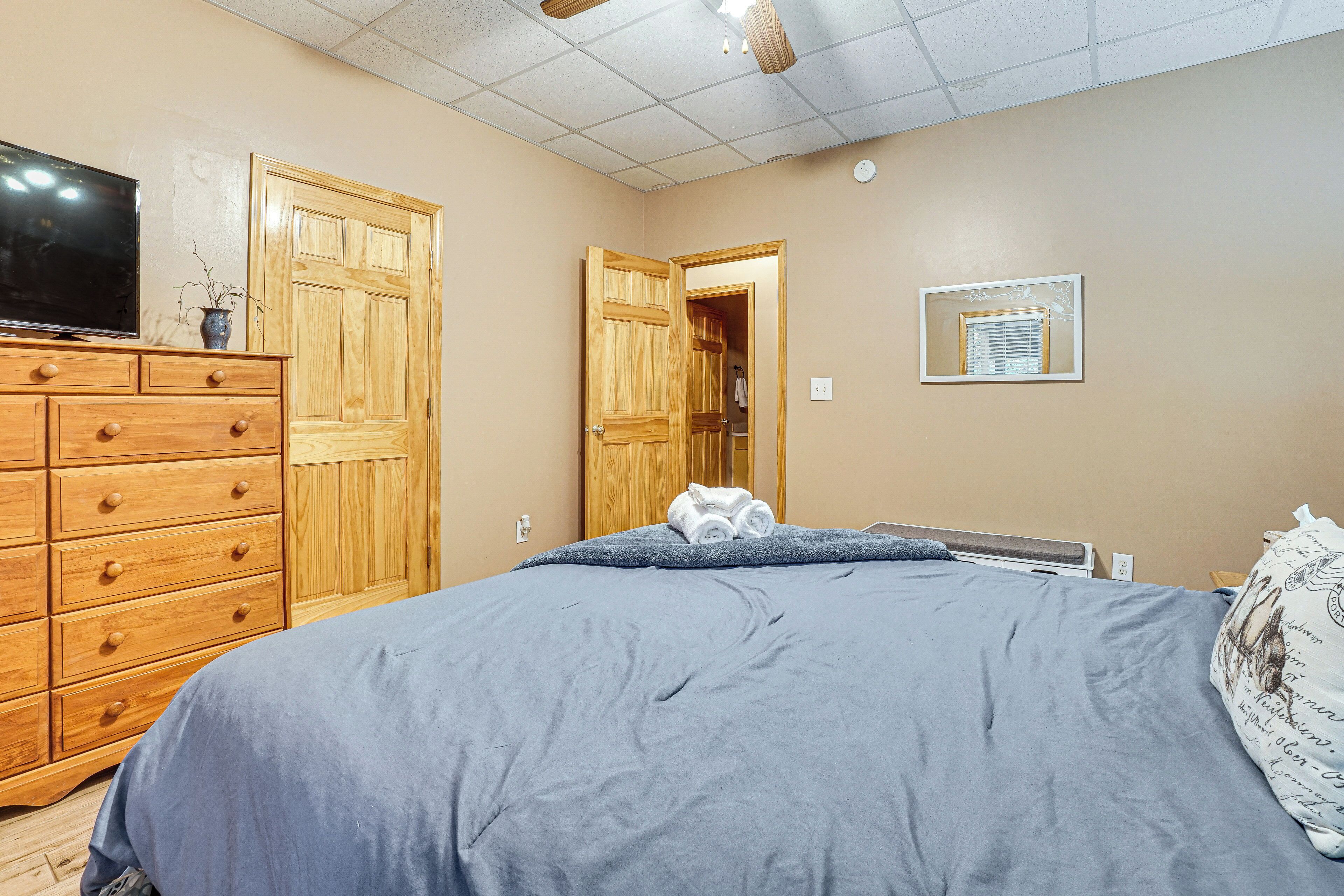 A bedroom with a bed, wooden dresser, television, and a door leading to another room.