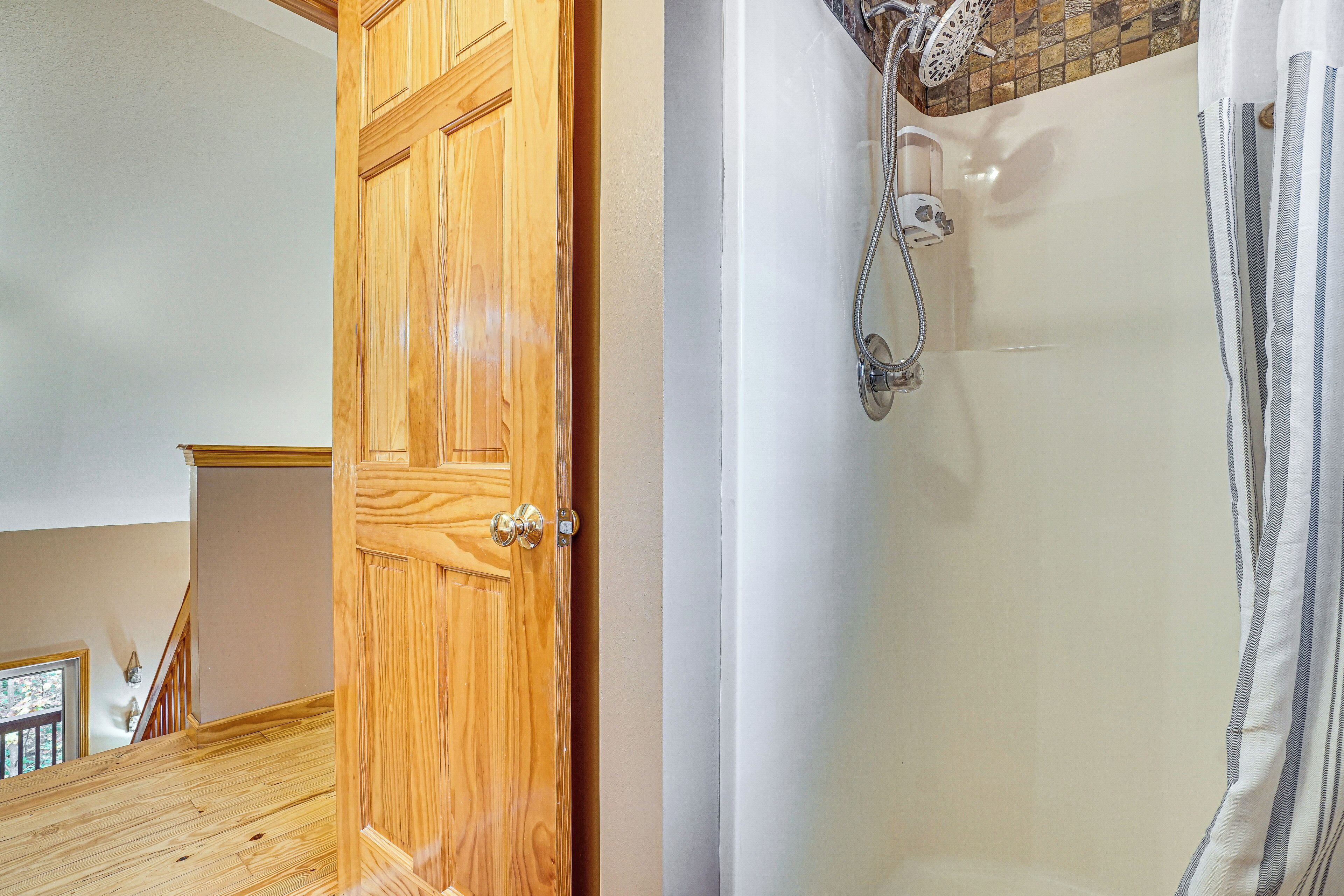 Puerta de madera que da a un baño con ducha y pared de azulejos.
