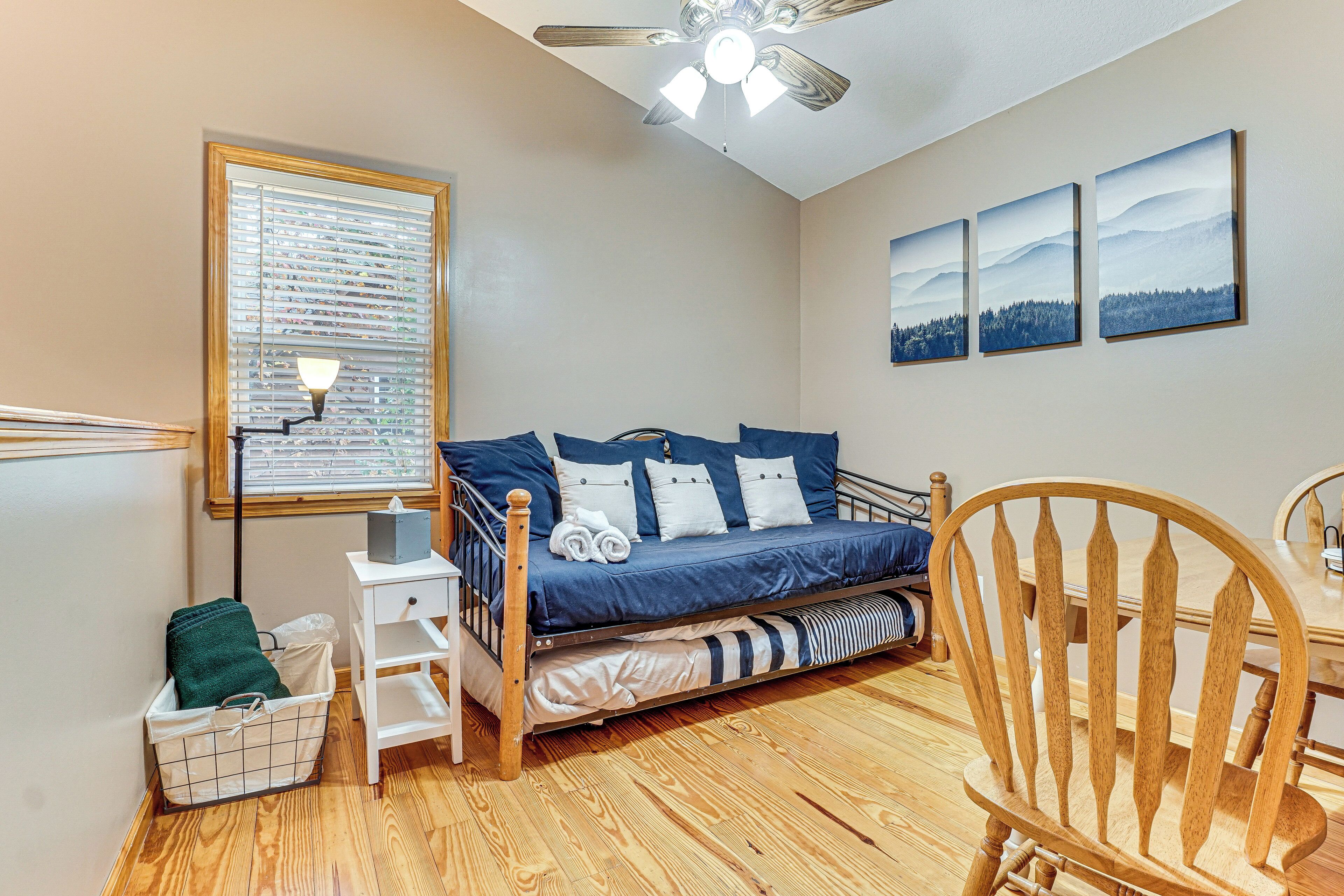 A bedroom with a bed, a chair, a wooden floor, a ceiling fan, and a window with blinds.