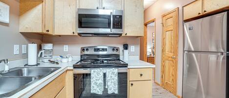 Una cocina con armarios de madera, electrodomésticos de acero inoxidable, incluyendo un microondas, estufa y refrigerador, y salpicadero de azulejos.