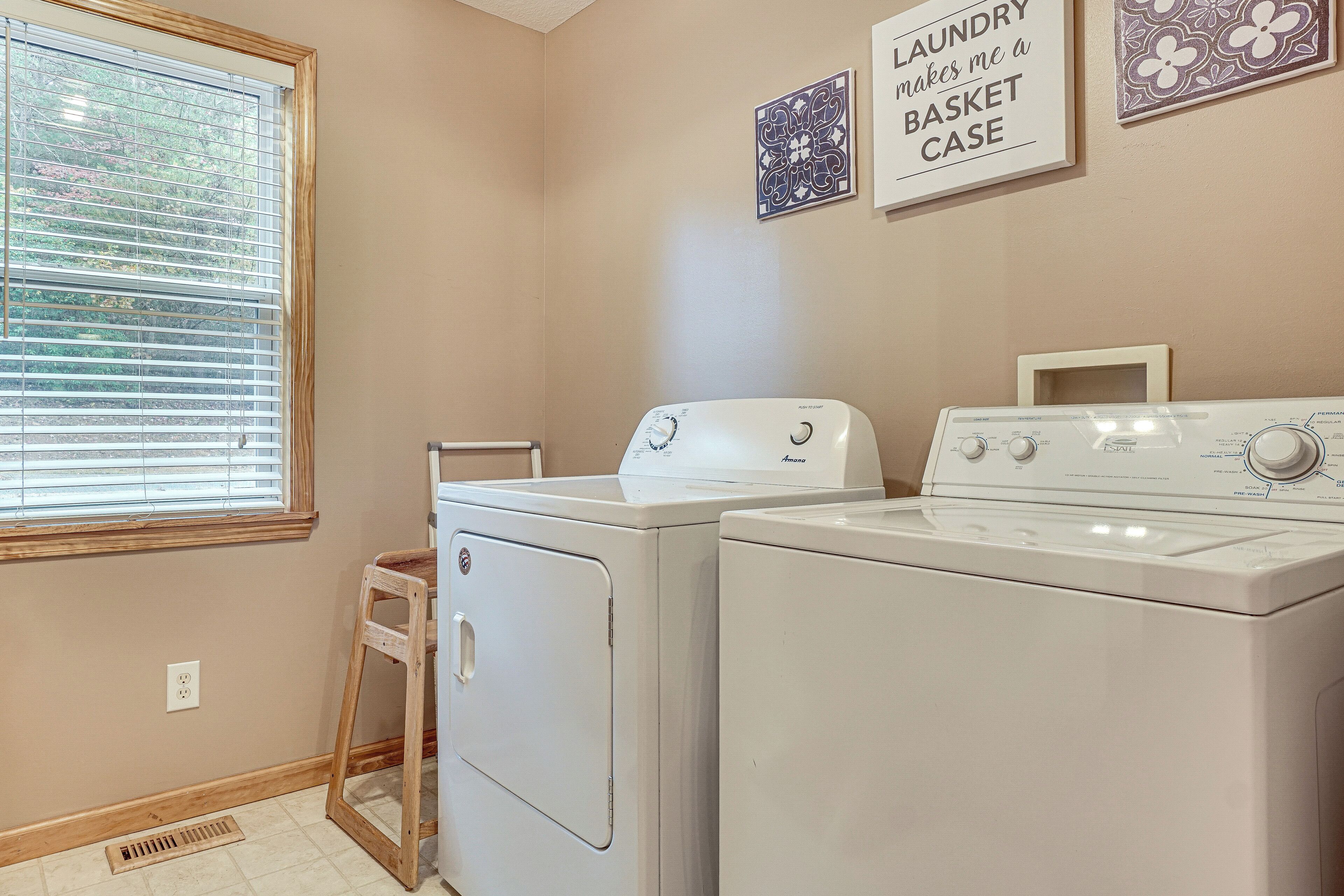 A laundry room with two white front-loading washers and dryers, a wooden step stool, and a vent.
