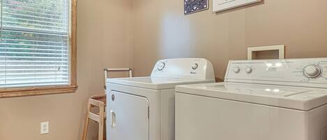 A laundry room with two white front-loading washers and dryers, a wooden step stool, and a vent.