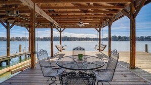 A covered outdoor deck with a round metal table and four chairs, overlooking a calm lake. - Lake Sinclair Retreat w/ Big Water Views & Dock! (Milledgeville)