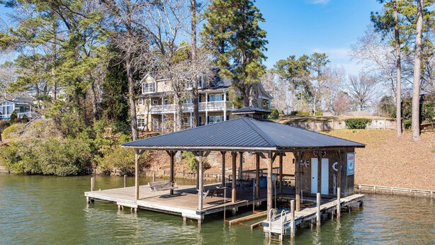 A wooden dock with a covered seating area and a small building with a sign, surrounded by trees and a house in the background. - Lake Sinclair Retreat w/ Big Water Views & Dock! (Milledgeville)