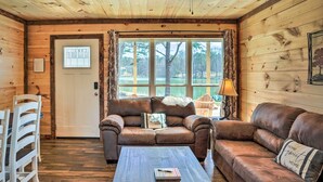 Ein gemütliches Blockhaus-Interieur mit Holzboden, einem braunen Ledersofa, einem Couchtisch und einem Fenster mit Seeblick.