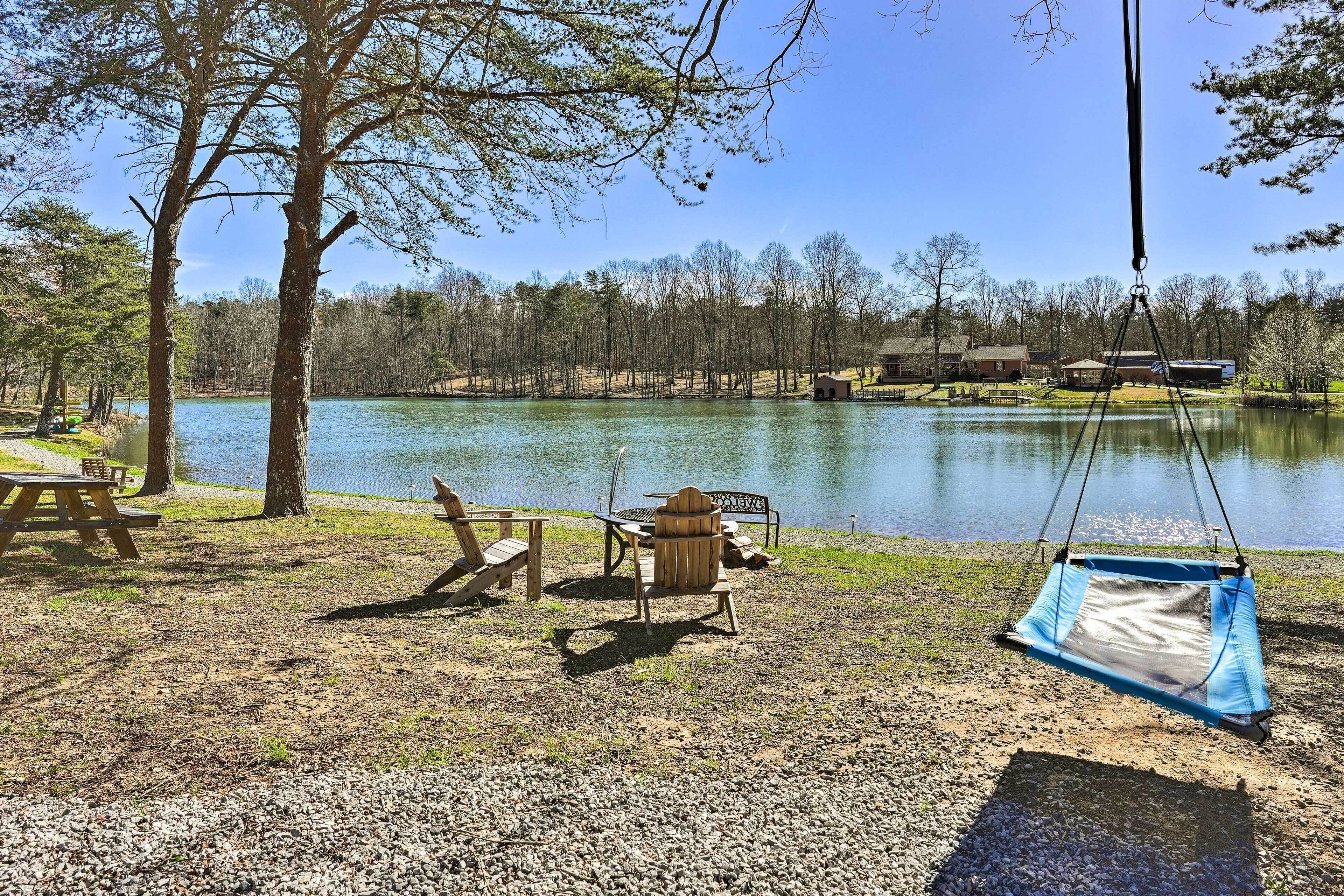 A lakeside camping area with picnic tables, chairs, and a hammock.