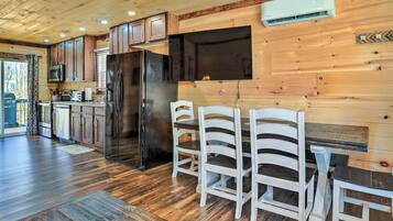 Une cuisine moderne avec des meubles en bois, un réfrigérateur noir et un coin repas avec des chaises blanches.