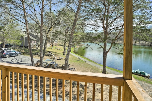 Terraza de madera con vistas a un lago, mesas de picnic y un muelle para embarcaciones.