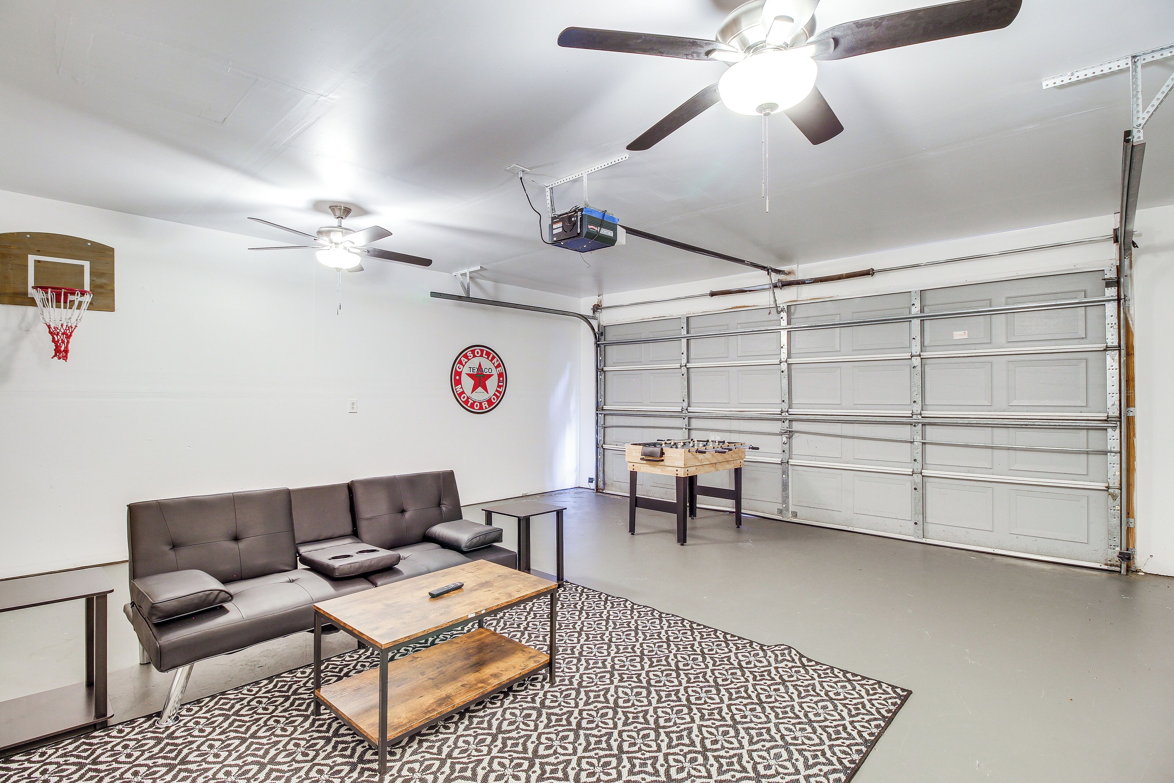 Een garage met een grijze bank, een salontafel, een kamerkleed met patroon, een plafondventilator en een aan de muur bevestigde projector.