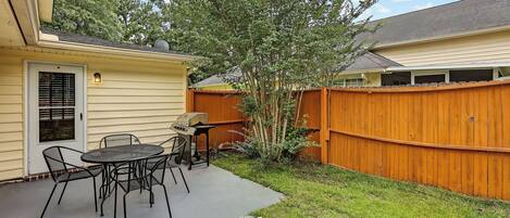 A backyard with a patio table and chairs, a wooden fence, and a tree.