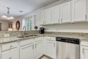 Uma cozinha moderna com armários brancos, bancadas de granito, lava-louças de aço inoxidável e máquina de café.