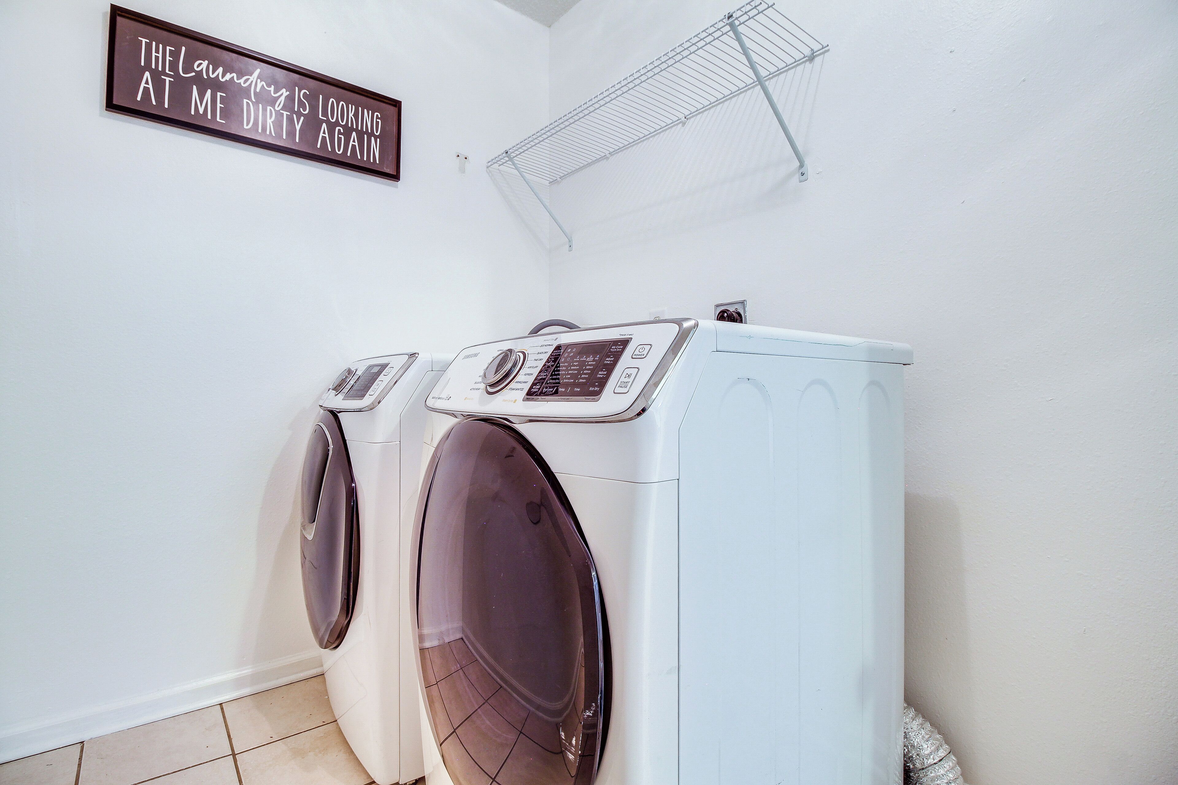 A laundry room with two front-loading washing machines, a drying rack, and a sign on the wall.