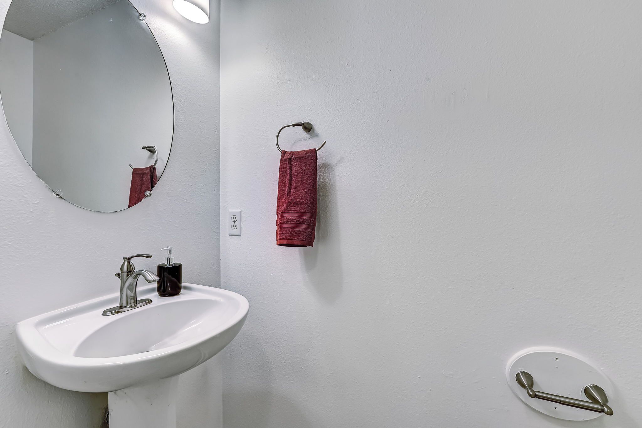 A bathroom with a white sink, a round mirror, a red towel, and a towel rack.