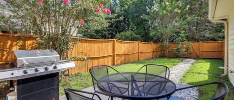 An outdoor patio with a grill, metal table, and chairs.
