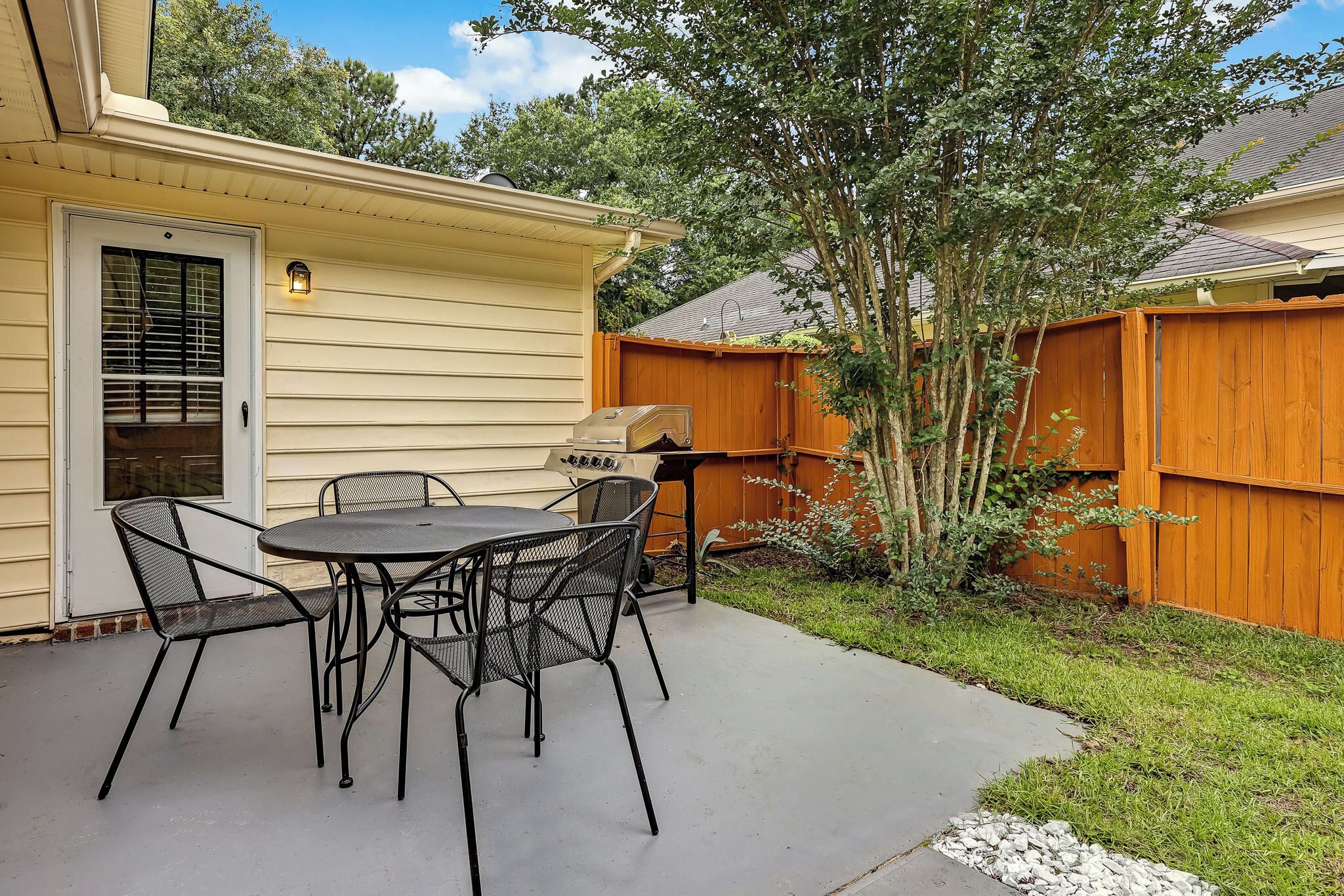 A patio with a table and chairs, a grill, and a wooden fence.