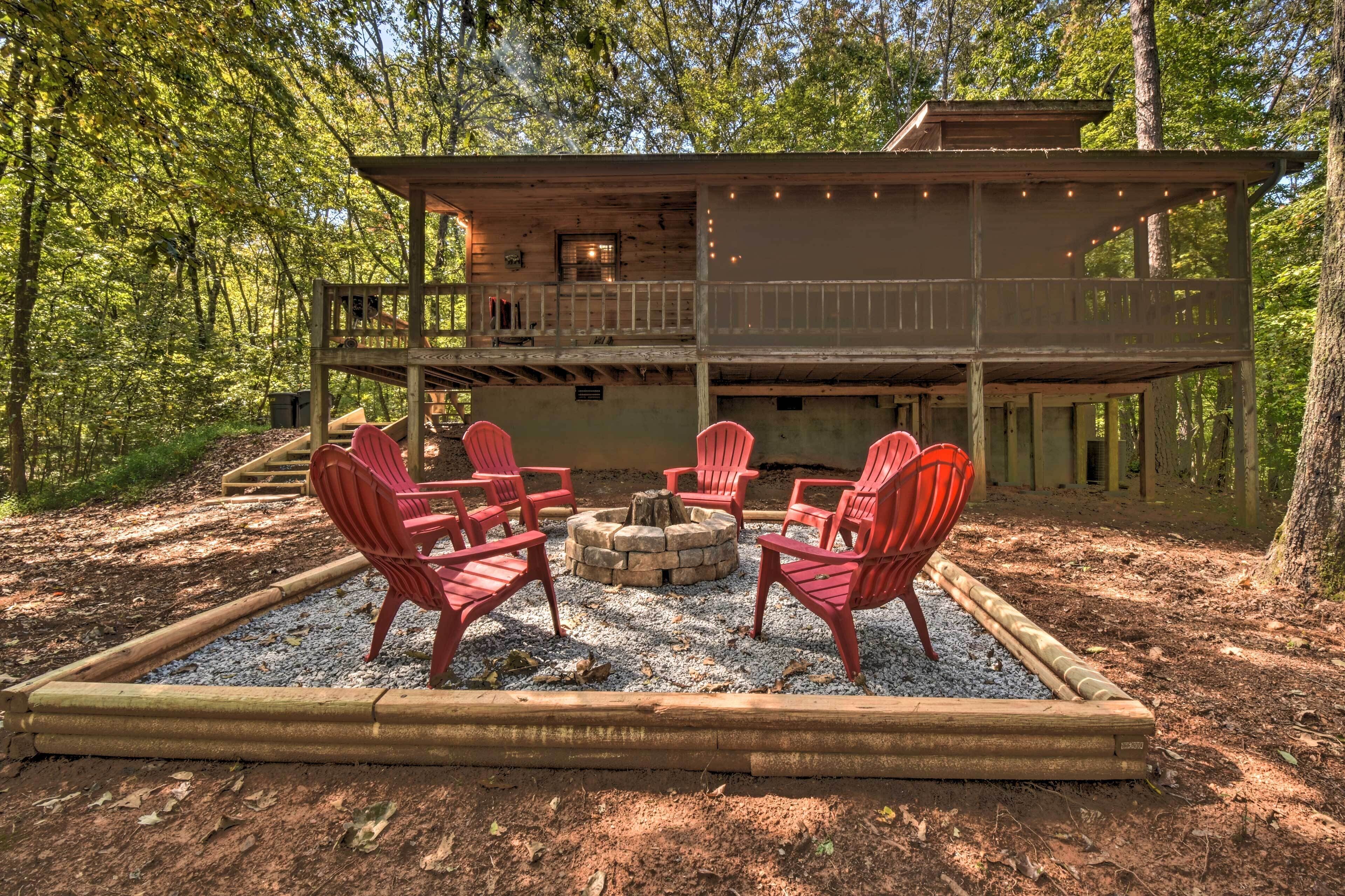Eine Hütte mit einer Terrasse, umgeben von einer Feuerstelle und roten Adirondack-Stühlen.