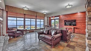 Ein geräumiges Wohnzimmer mit Ledersofas, einem Steinkamin, großen Fenstern mit Blick auf die Berge und einer Wand als Steinakzent.